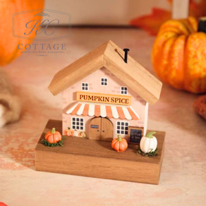 Wooden house-shaped pumpkin spice container with pumpkins around on a soft surface.