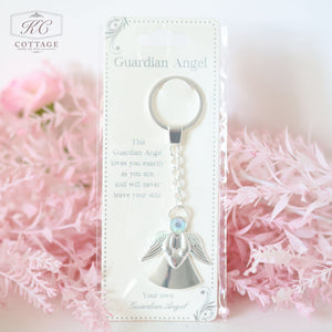 A packaged Gift Set - Best Friend with a metallic angel charm and a keyring, placed against a backdrop of pink flowers. The label reads, "This Guardian Angel loves you exactly as you are, and will never leave your side." Perfect as a meaningful piece of home decor.