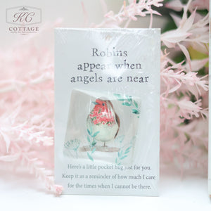 A small card with the text "Robins appear when angels are near" and an illustration of a robin. Below, it reads, "Here's a little pocket hug just for you. Keep it as a reminder of how much I care, for the times when I cannot be there." Surrounded by delicate pink foliage, Pocket Hugs with Sentiments is perfect for home decor.