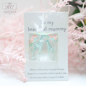 A Pocket Hugs with Sentiments card with "To my beautiful mummy" printed on it, featuring an illustration of two giraffes and a sentiment: "Here's a little pocket hug just for you. Keep it as a reminder of how much I care, for the times when I cannot be there." The pink floral background makes it perfect for home decor.