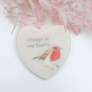 A Marble Pocket Pebble Robin Sentiment Heart with an illustration of a red-breasted robin and the text "Always in our hearts." The background features soft pink foliage, making it a perfect piece for home decor.