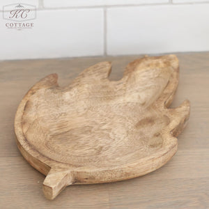 A Mango Wood Leaf Tray, crafted with a leaf design, is displayed on a wooden surface against a backdrop of white tiles. The tray showcases a natural wood finish and detailed grain patterns, radiating organic elegance. In the upper left corner, the "KC Cottage" logo is visible. Ideal for home decor enthusiasts.