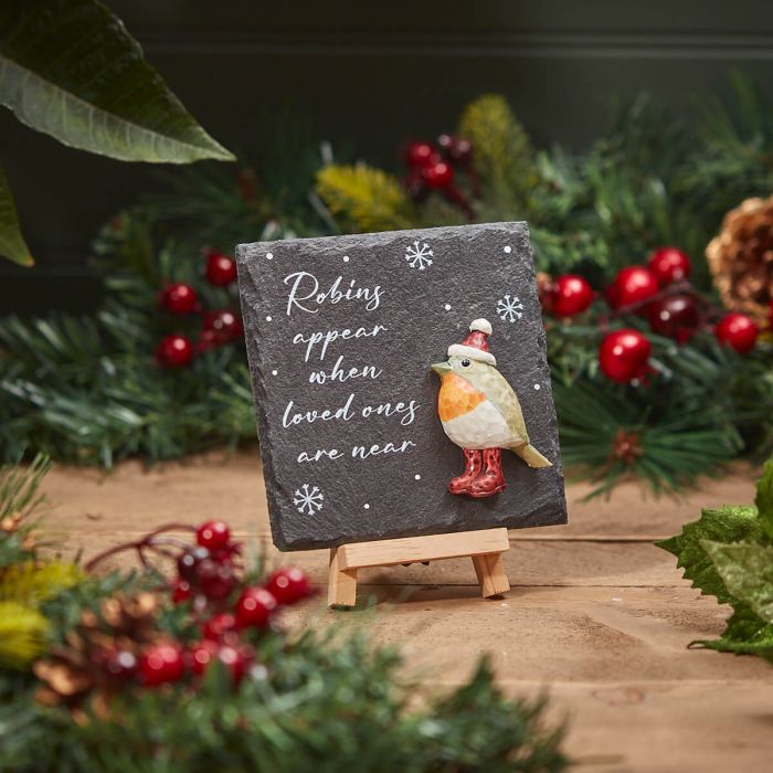 The Christmas Slate Robins Appear Easel Plaque features a small, decorative design surrounded by festive Christmas greenery and berries. It showcases a cute robin adorned with a hat and scarf, accompanied by the heartfelt text, "Robins appear when loved ones are near," set against a dark background embellished with snowflakes. This charming piece brings holiday cheer to any space.