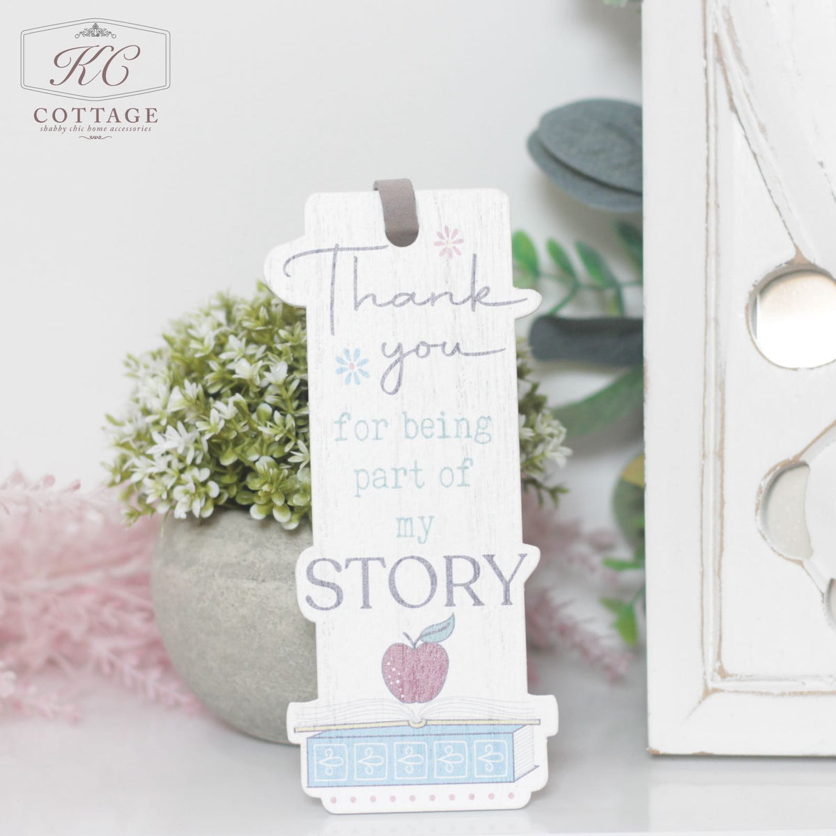 A Teacher Gift - Thank You Bookmark with text reading "Thank you for being part of my story," featuring pastel colors and a small apple graphic at the bottom. It is set against a background of plants and home decor.