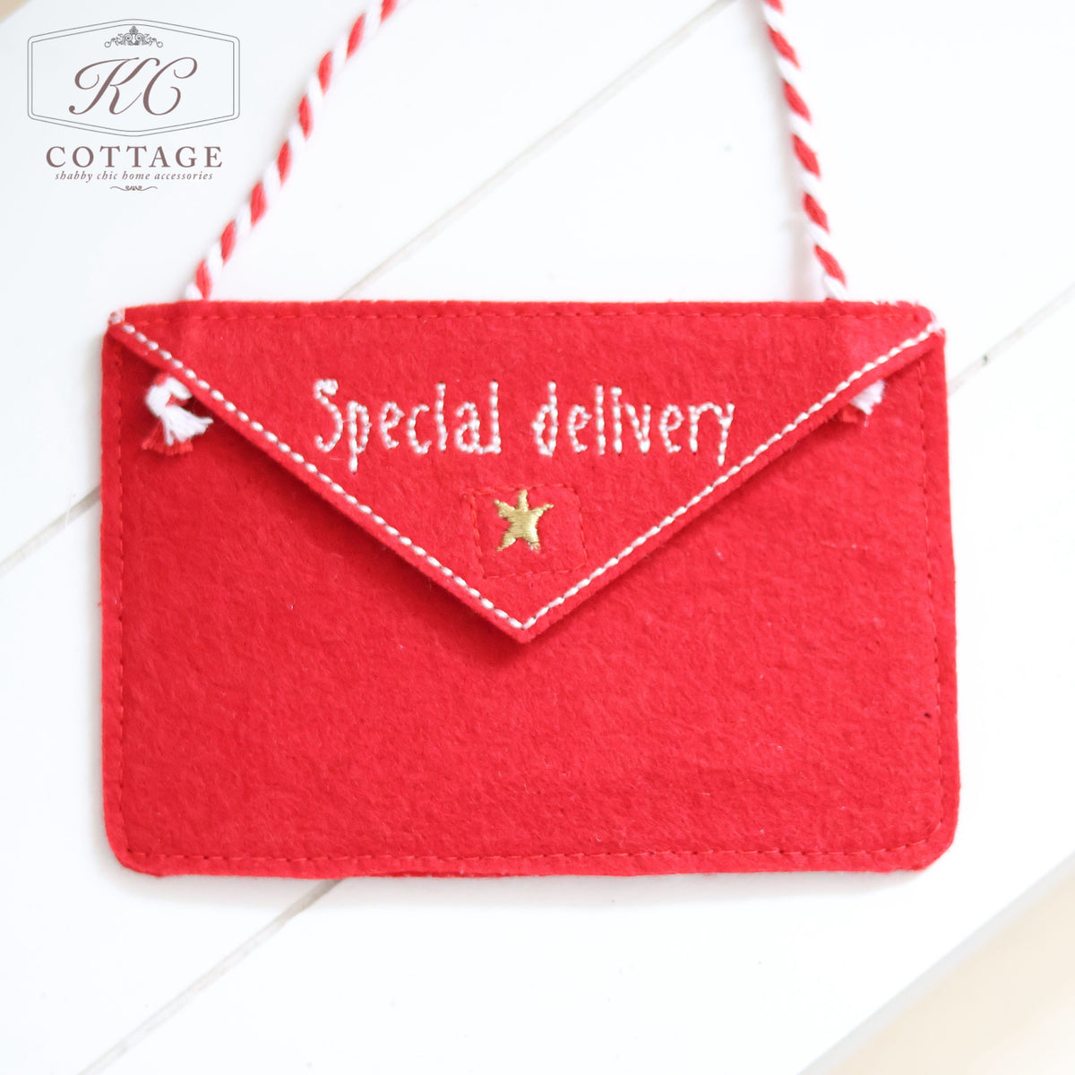 The Christmas Hanging Santa Envelopes are red felt envelopes accented with white stitching and a star detail, labeled "Special delivery." They make ideal Christmas ornaments or letters to Santa, hanging by a red and white striped string. The KC Cottage logo is positioned in the top left corner against a white wooden surface.