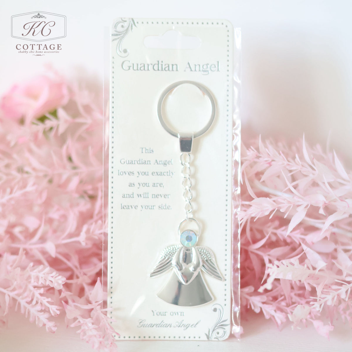 A packaged Gift Set - Best Friend with a metallic angel charm and a keyring, placed against a backdrop of pink flowers. The label reads, "This Guardian Angel loves you exactly as you are, and will never leave your side." Perfect as a meaningful piece of home decor.