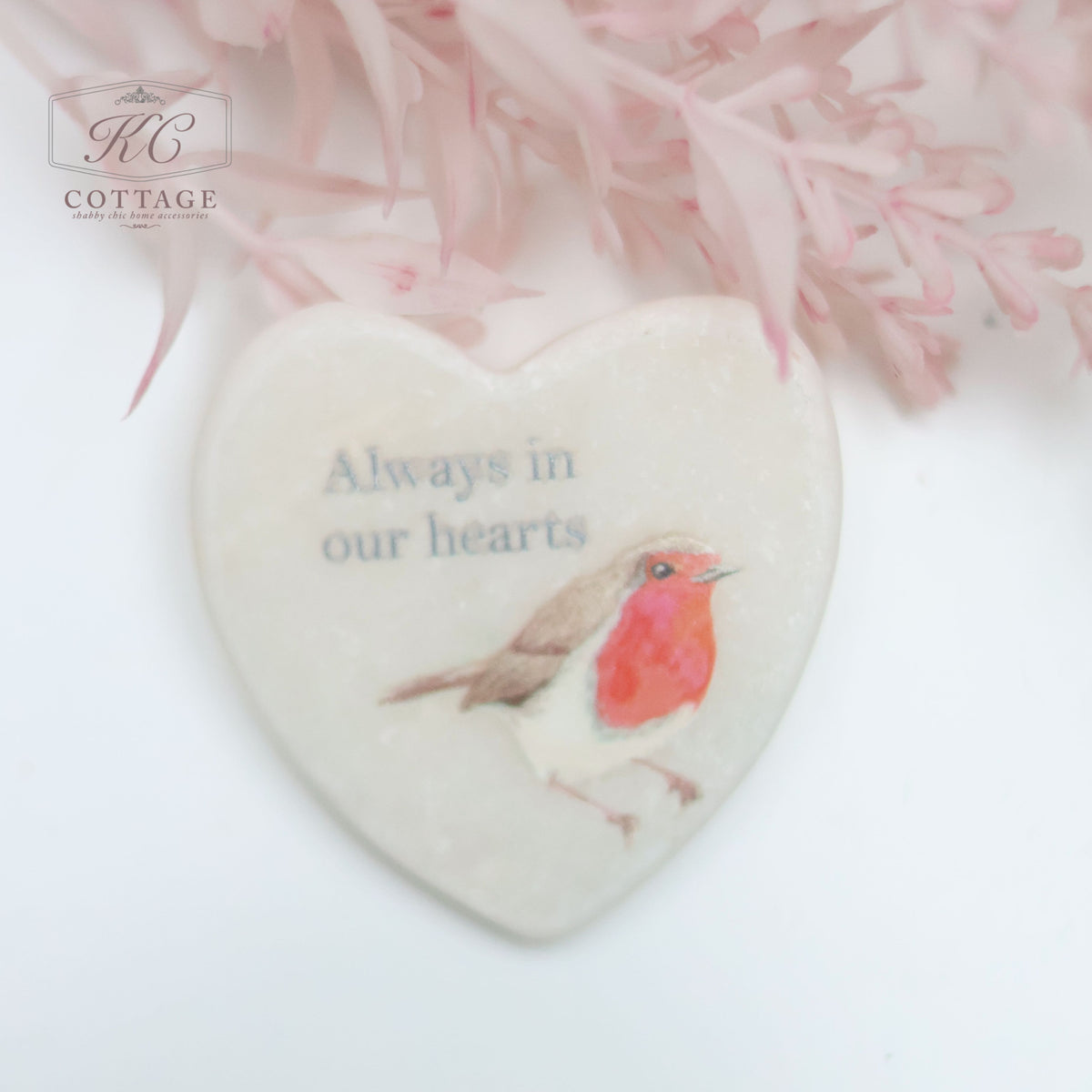 A Marble Pocket Pebble Robin Sentiment Heart with an illustration of a red-breasted robin and the text "Always in our hearts." The background features soft pink foliage, making it a perfect piece for home decor.