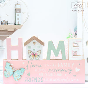 A charming piece of home decor, the Bright Butterfly Wooden Signs - Family, Friend, Home spells "HOME" with pastel-colored letters, where the "O" is represented by a small house. Adorned with butterfly illustrations, it reads, "Home is where family belongs, memories are created, and friends are always welcome.