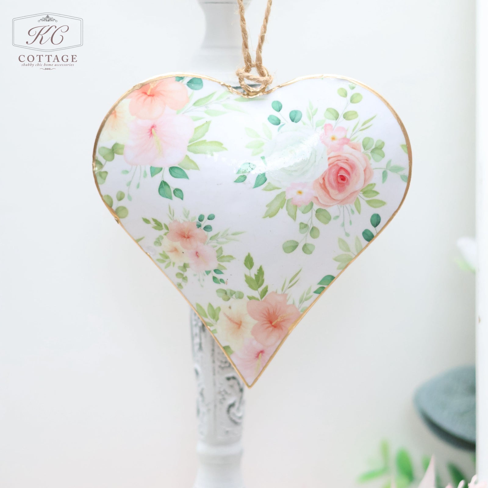 A **Pink Floral Hanging Heart**, perfect for home decor, features a floral pattern with pink roses and green leaves, hanging by a twine. The white background enhances its charm.