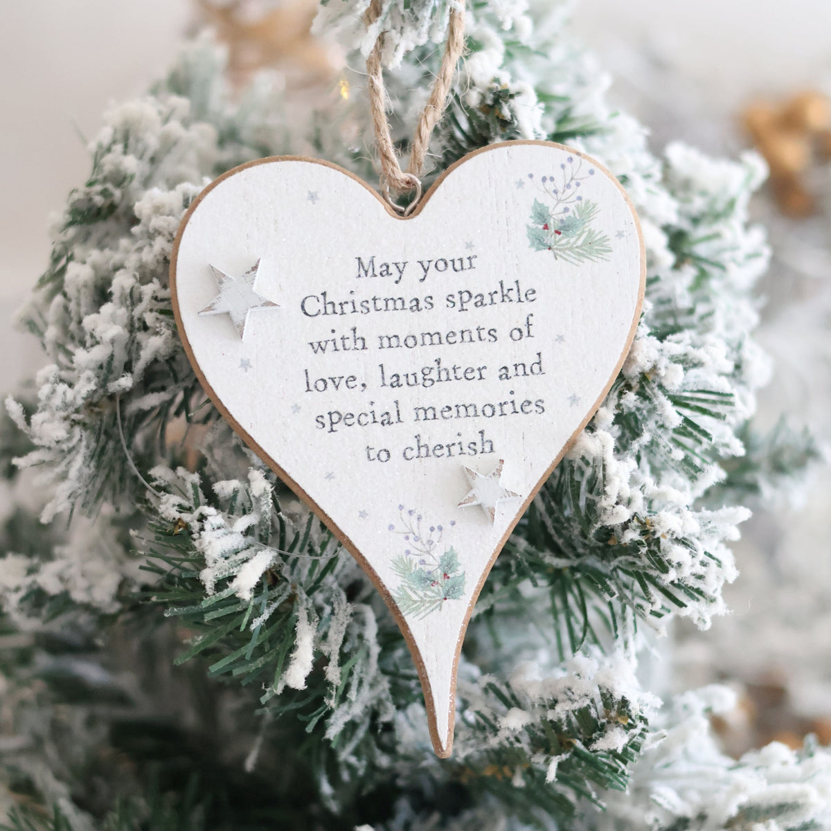 A Christmas Sentiment Heart Hanger With 3D Star, featuring the message "May your Christmas sparkle with moments of love, laughter, and special memories to cherish," hangs on a frosted Christmas tree. Adorned with festive illustrations and a 3D star, this ornament adds cozy holiday joy to your decor.