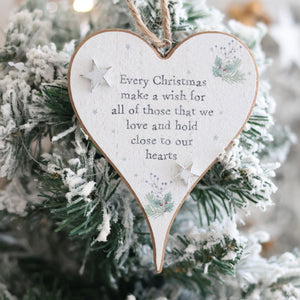 The Christmas Sentiment Heart Hanger With 3D Star, adorned with the inscription "Every Christmas make a wish for all of those that we love and hold close to our hearts," hangs on a snow-dusted Christmas tree. Decorated with small stars and pine branches, it radiates festive joy.