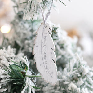 A silver feather-shaped ornament engraved with the words "Merry Christmas to our angel" hangs on a snow-covered Christmas tree branch, becoming a cherished memory in our Christmas Family Sentimental Feather Hanger collection.