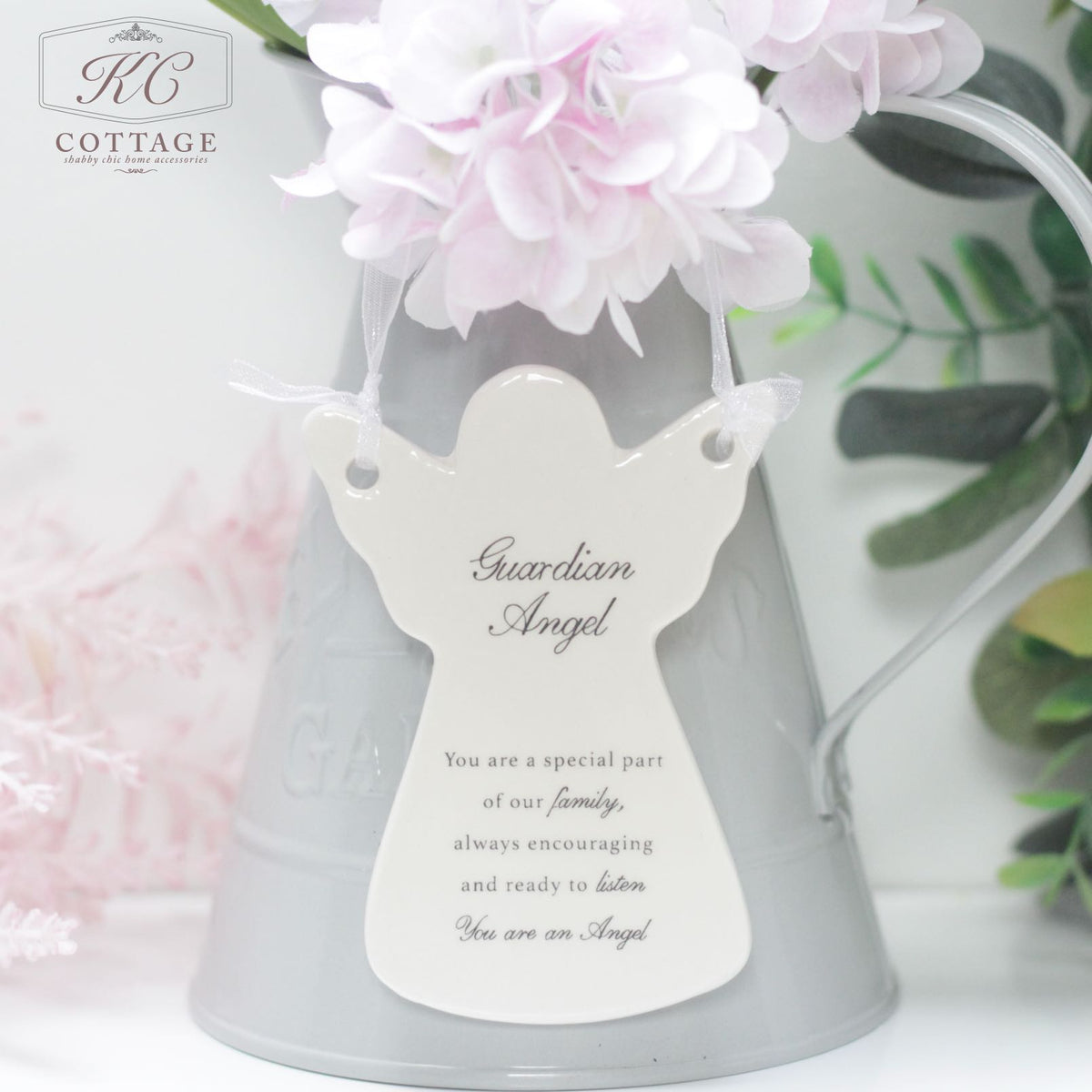 A Ceramic Guardian Angel Hanging Ornament with a message hangs on a gray pitcher adorned with light pink flowers. The message reads: "Guardian Angel. You are a special part of our family, always encouraging and ready to listen. You are our Angel." As an elegant piece of home decor.