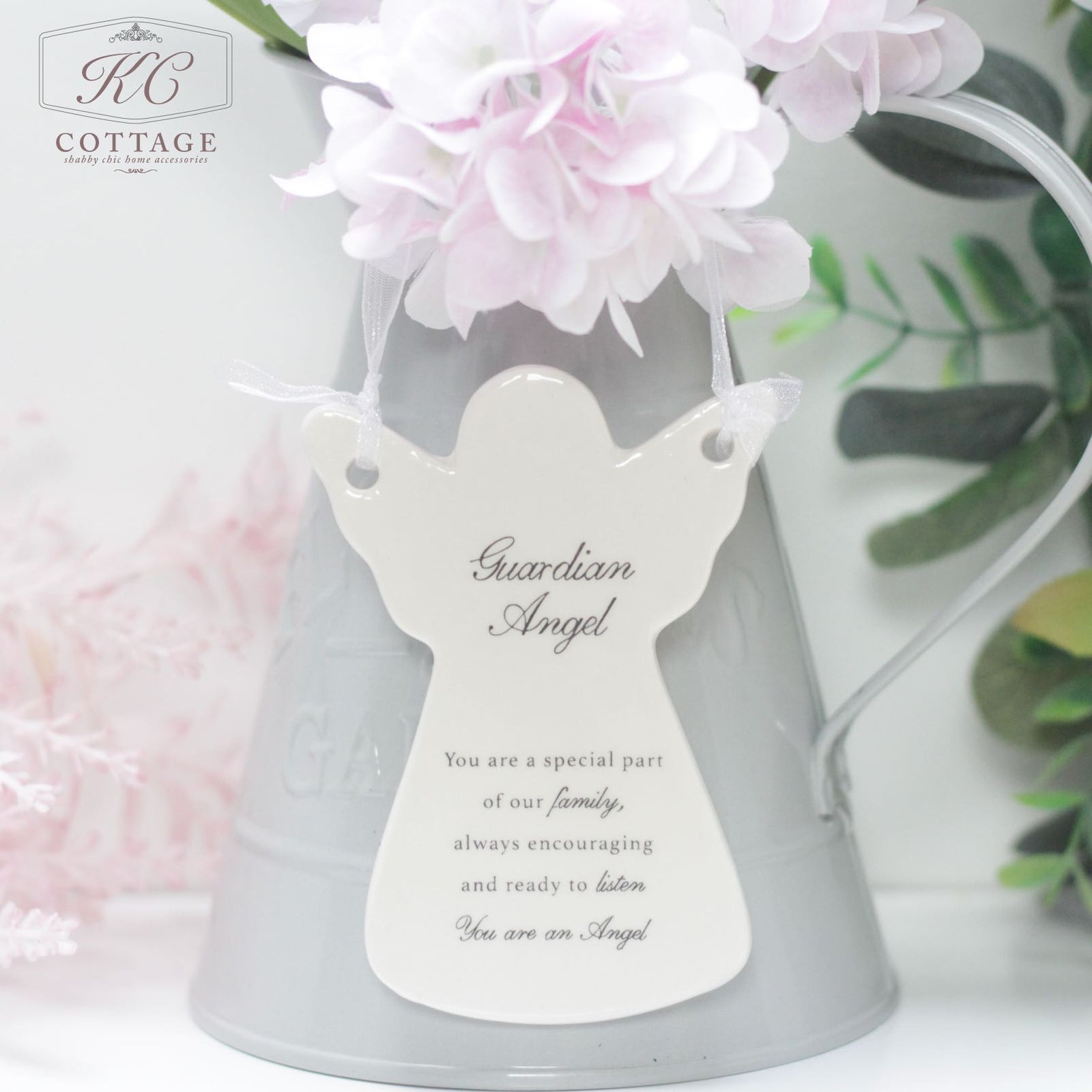 A Ceramic Guardian Angel Hanging Ornament with a message hangs on a gray pitcher adorned with light pink flowers. The message reads: "Guardian Angel. You are a special part of our family, always encouraging and ready to listen. You are our Angel." As an elegant piece of home decor.