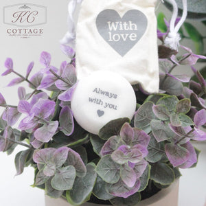 A potted plant with purple and green leaves is shown with a round white stone bearing the words "Always with you" alongside a small cloth pouch labeled "Marble Sentiment Tokens in gift bag" featuring a heart design. This elegant piece makes a perfect addition to your home decor.