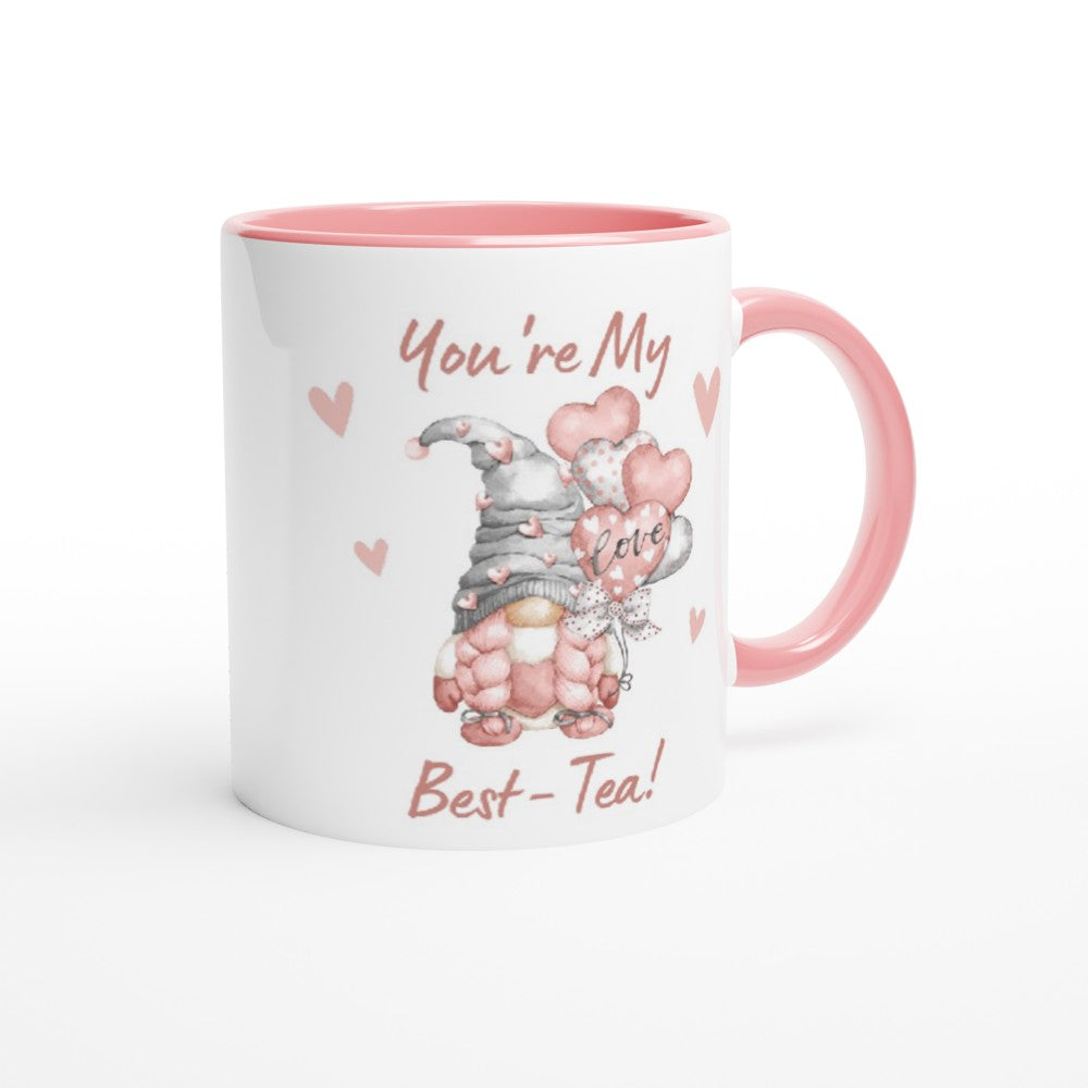 A white and pink "You're My Best-tea Gonk Mug" with a whimsical gnome holding heart-shaped balloons, perfect for adding charm to your home decor. The mug features pink text that reads "You're My Best-Tea!" with small hearts decorating the design. The gnome and text are in shades of pink and grey.
