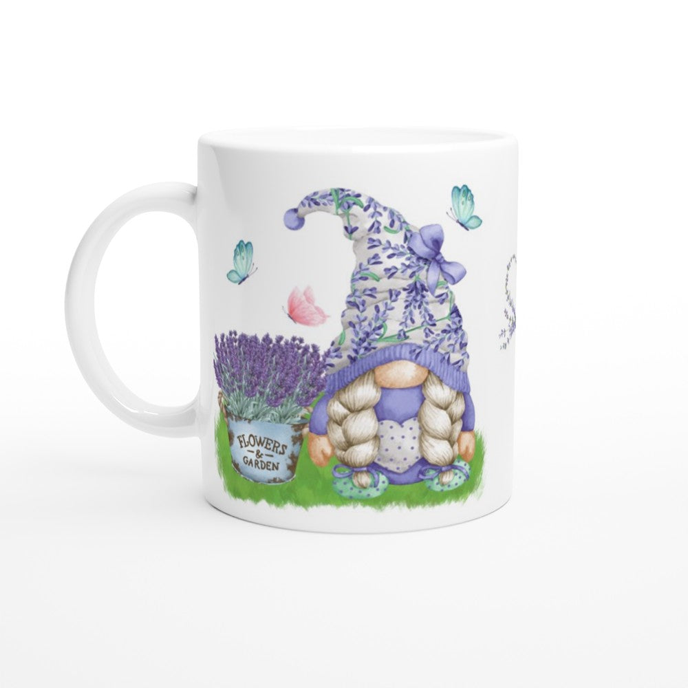 A Gonk Lavender & Butterfly Mug featuring an illustration of a gnome with long braids wearing a lavender-themed hat. The gnome is surrounded by lavender sprigs and butterflies, with a sign that reads "Flower Garden." Perfect for adding charm to your home decor.