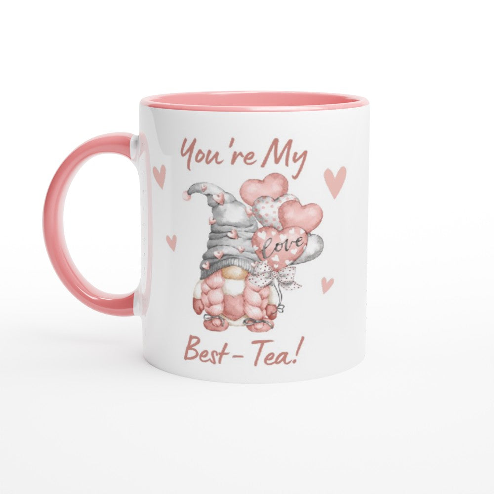 A white and pink You're My Best-tea Gonk Mug with an illustration of a gnome holding heart-shaped balloons that say "love." Surrounding the gnome are small pink hearts. The text on the mug reads, "You're My Best-Tea!" Perfect for adding a touch of whimsical charm to your home decor.