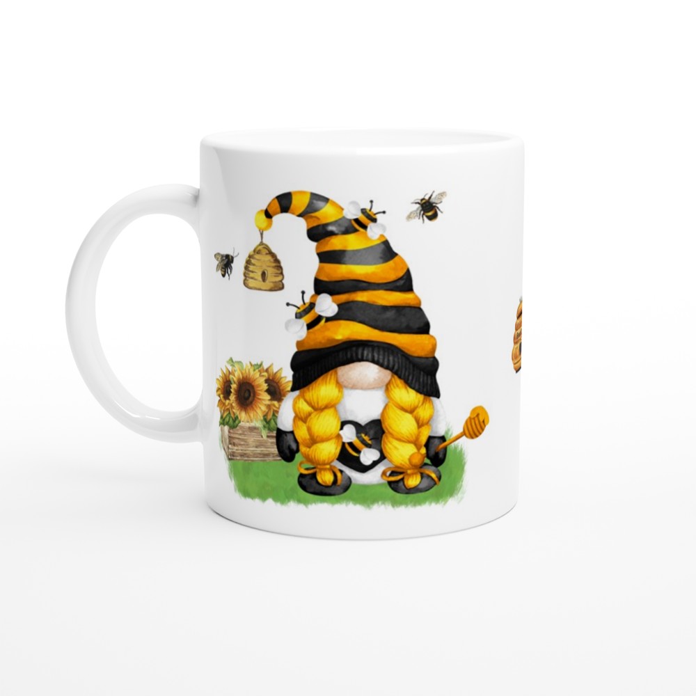 This Bee & Sunflower Gonk Mug, perfect for home decor, features a cute gnome wearing a black and yellow striped hat resembling a bee. The gnome has long yellow braids, holds a honey dipper, and stands on grass near sunflowers, a beehive, and buzzing bees.